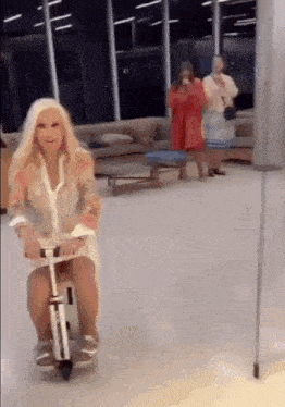 a woman is riding a scooter in a room with other women standing behind her .