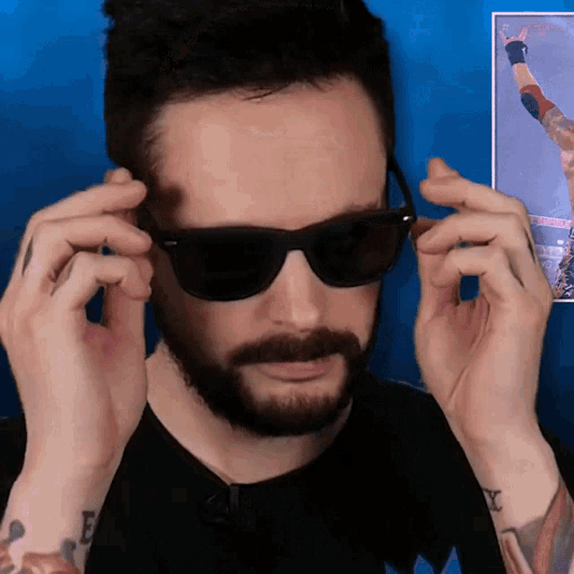 a man with a beard is wearing sunglasses in front of a picture of a man with a tattoo on his arm