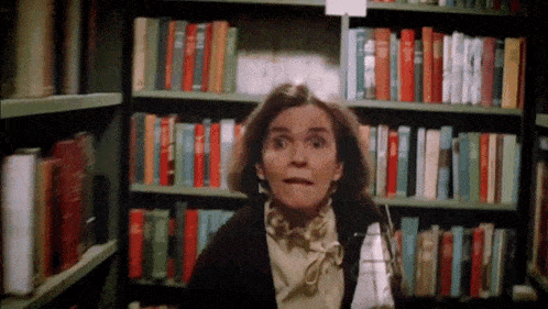 a woman is standing in front of a bookshelf with a sign that says ' a ' on it