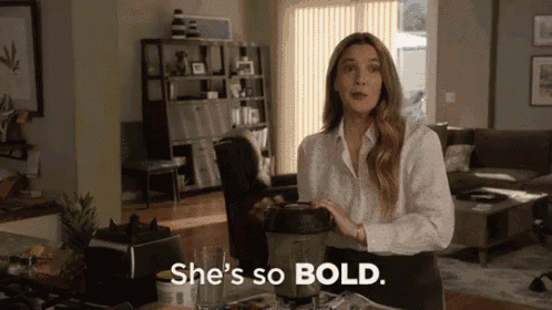 a woman is standing in a living room holding a blender and saying she 's so bold