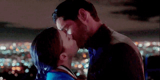 a man and woman are kissing in front of a city skyline at night .