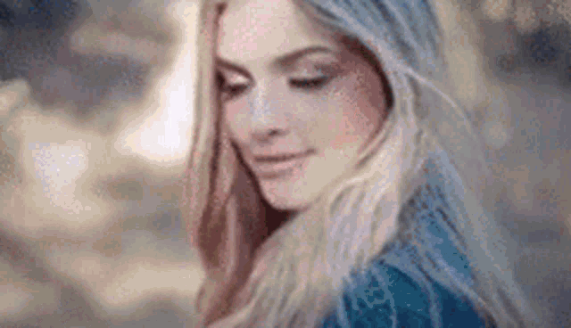 a close up of a woman with long blonde hair wearing a blue shirt .