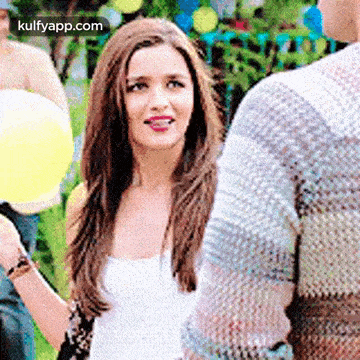 a woman in a white tank top is holding a yellow balloon and talking to a man .