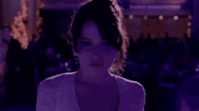 a woman in a white dress is standing in front of a crowd of people in a dark room .