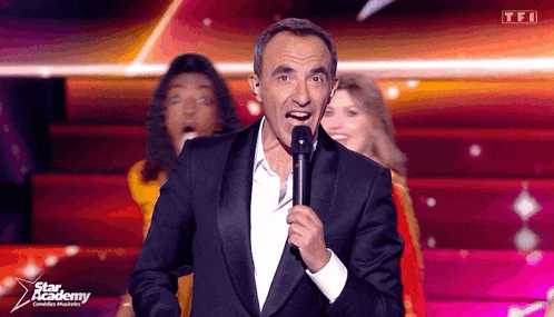 a man in a tuxedo is singing into a microphone with the words star academy on the bottom right