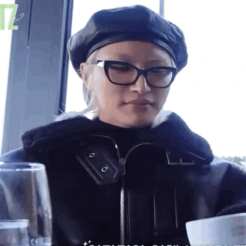 a woman wearing glasses and a leather jacket is sitting at a table with a glass of wine .