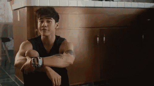 a young man with a tattoo on his arm is sitting in front of a counter .