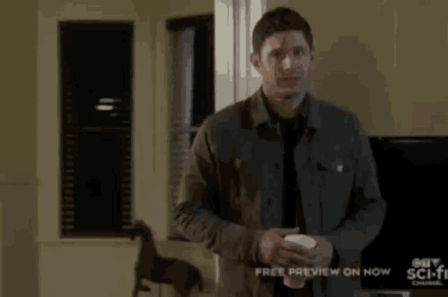 a man in a jacket and tie is holding a cup of coffee in a living room .