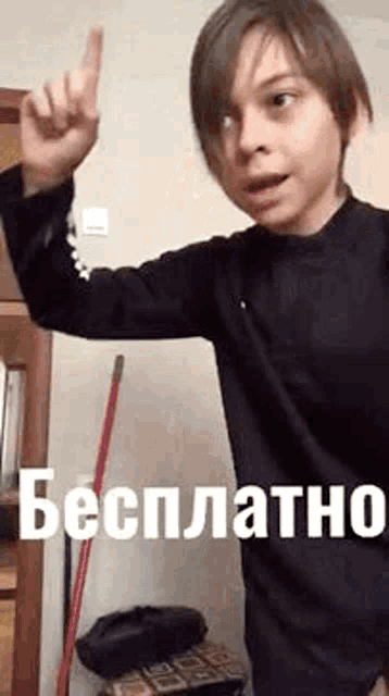 a young boy in a black shirt is standing in front of a mop and pointing up .