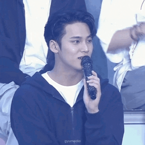 a young man is holding a microphone in his hand and looking at the camera .
