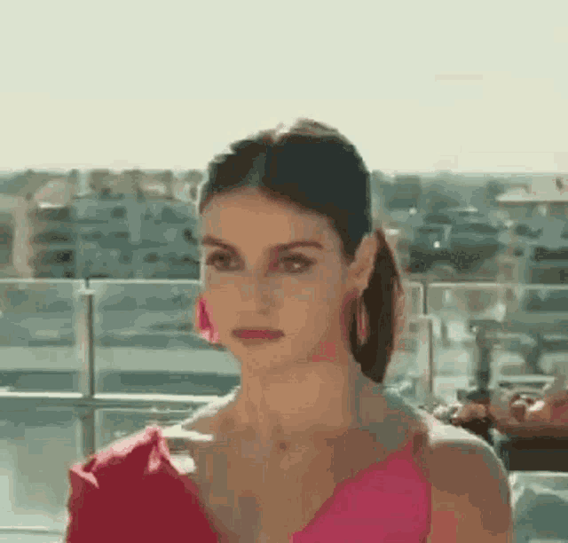 a woman in a pink dress and pink earrings is standing on a balcony .