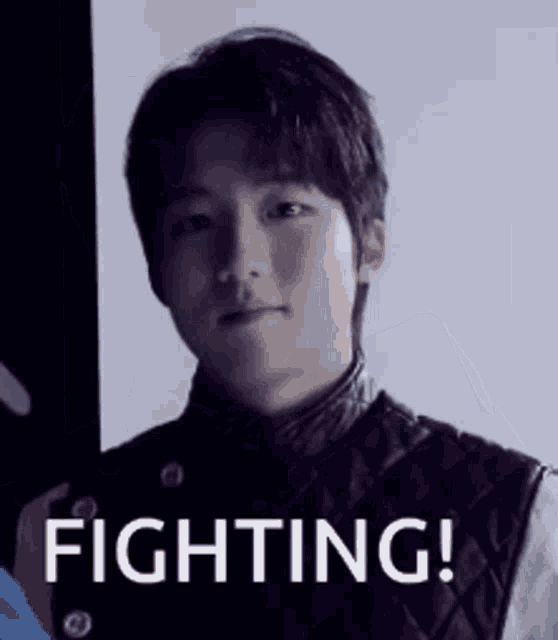 a man is standing in front of a wall with the words `` fighting ! '' written on it .