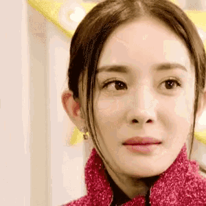 a close up of a woman 's face with a pink jacket and earrings .