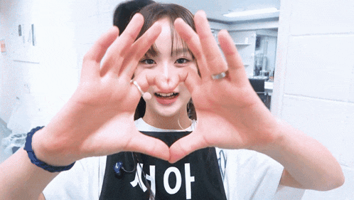 a girl making a heart shape with her hands wearing a shirt that says ' aoi ' on it