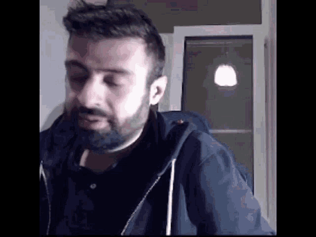 a man with a beard is standing in front of a window and looking at the camera .
