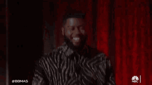 a man in a zebra print jacket is smiling and clapping his hands .