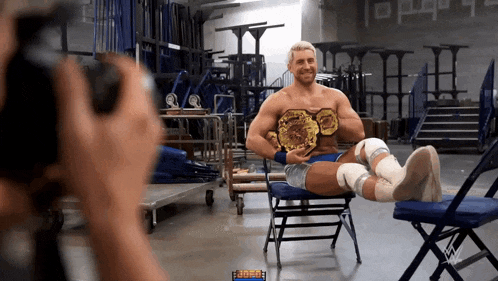 a wrestler is sitting in a chair with his legs crossed while a camera takes a picture of him