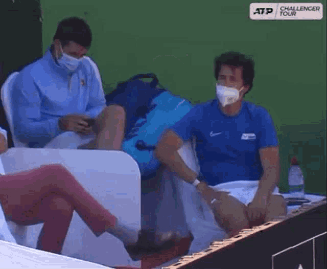 a man wearing a mask sits next to another man wearing a blue shirt with the word challenger on it