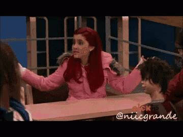 a girl with red hair and a pink jacket is sitting at a table .