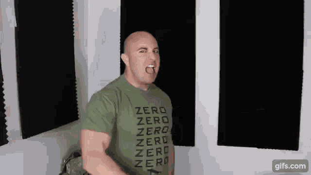 a bald man wearing a green t-shirt that says `` zero '' is standing in front of a wall .