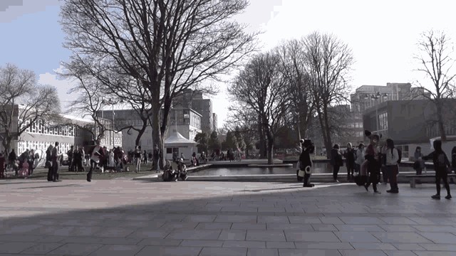 a group of people are gathered in a park with trees and a building in the background