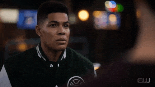 a man wearing a green and white varsity jacket with a circle on the front