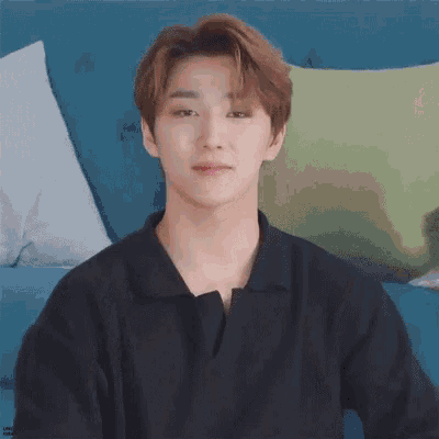 a young man in a black shirt is sitting on a couch with pillows .