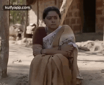 a woman in a saree is sitting on the ground with her arms around her waist .