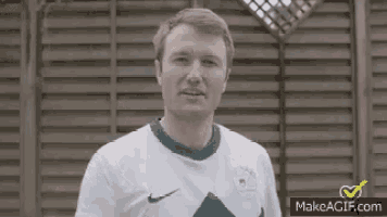 a man in a white and green nike shirt is standing in front of a wooden wall .