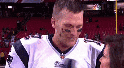 a man wearing a patriots jersey is standing next to a woman .