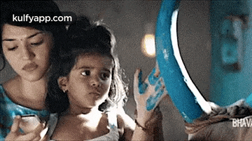 a woman is holding a little girl in her arms while looking at her hand in a mirror .