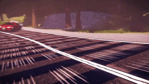 a red car is driving down a road with a shadow on the ground