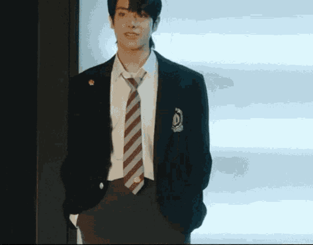 a young man in a school uniform and tie is standing in front of a window .