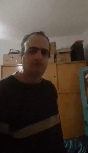 a man wearing glasses and a black shirt is standing in front of a wooden cabinet