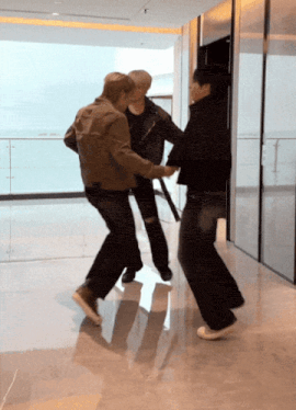 three men are dancing in a hallway and one of them is wearing white sneakers