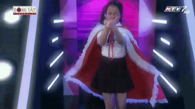 a girl in a red cape stands in front of a sign that says dong tay on it