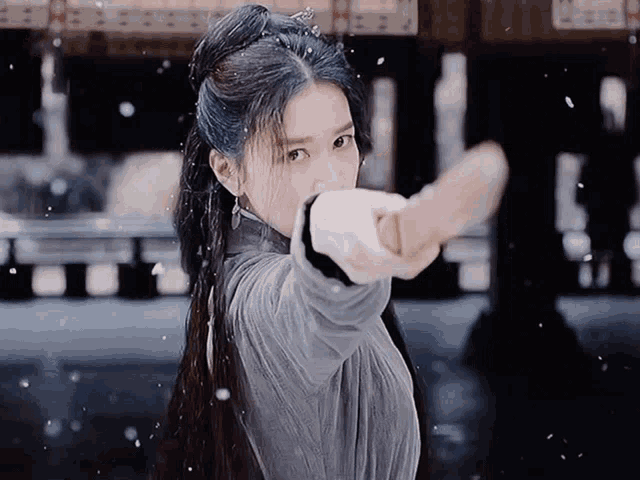 a woman in a gray dress is holding a sword in her hand