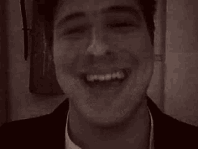 a man is laughing in front of a fire extinguisher in a black and white photo .