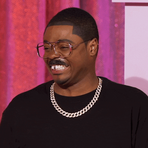 a man wearing glasses and a chain around his neck is smiling