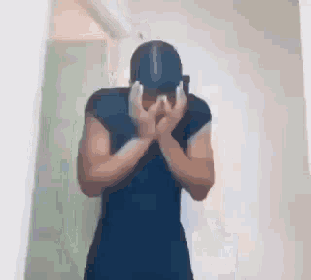a man is covering his face with his hands while wearing a hat .