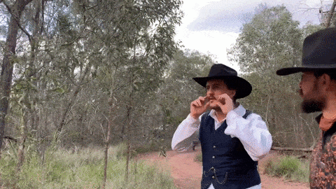 two men in cowboy hats are standing on a dirt road .