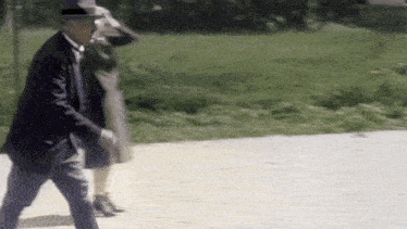 a man in a suit and hat is walking with a woman in a dress