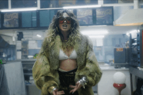 a woman wearing a fur coat and sunglasses stands in front of a coca cola sign