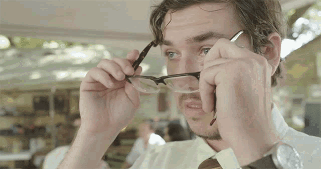 a man adjusts his glasses while wearing a wrist watch