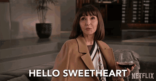 a woman sitting on a couch holding a glass of wine and saying hello sweetheart