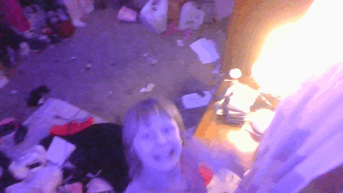 a girl is standing in a messy room with purple lights behind her