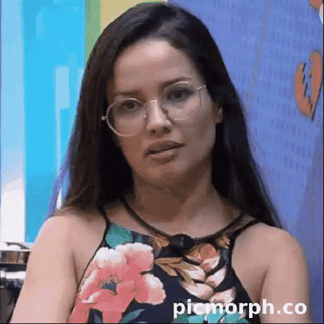 a woman wearing glasses and a floral top is making a funny face .