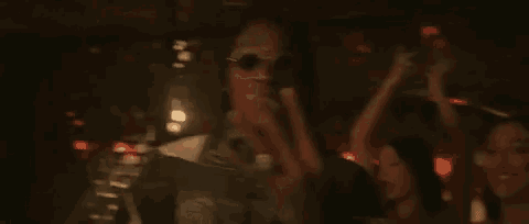 a man wearing sunglasses is standing next to a woman in a club .