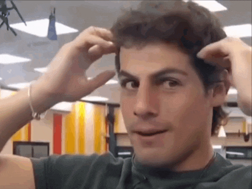 a man in a black shirt is adjusting his hair with his hands