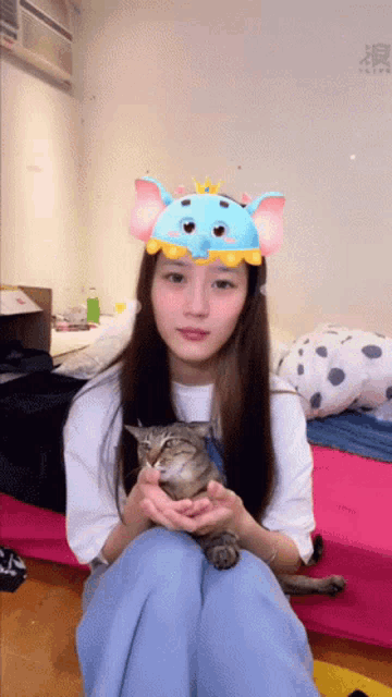 a woman wearing an elephant headband is holding a cat